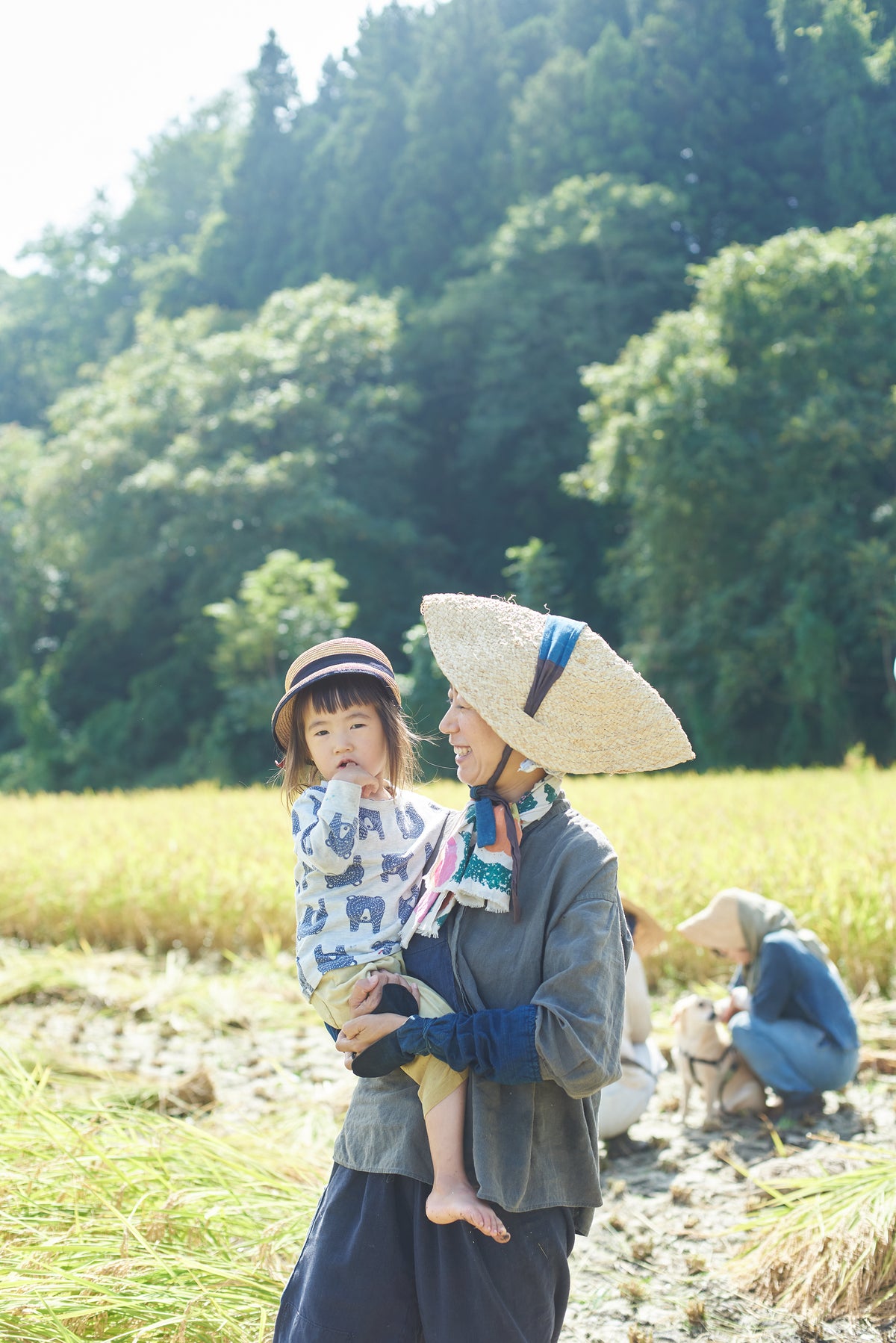 稲刈りの日、田んぼで子どもを抱く仲間